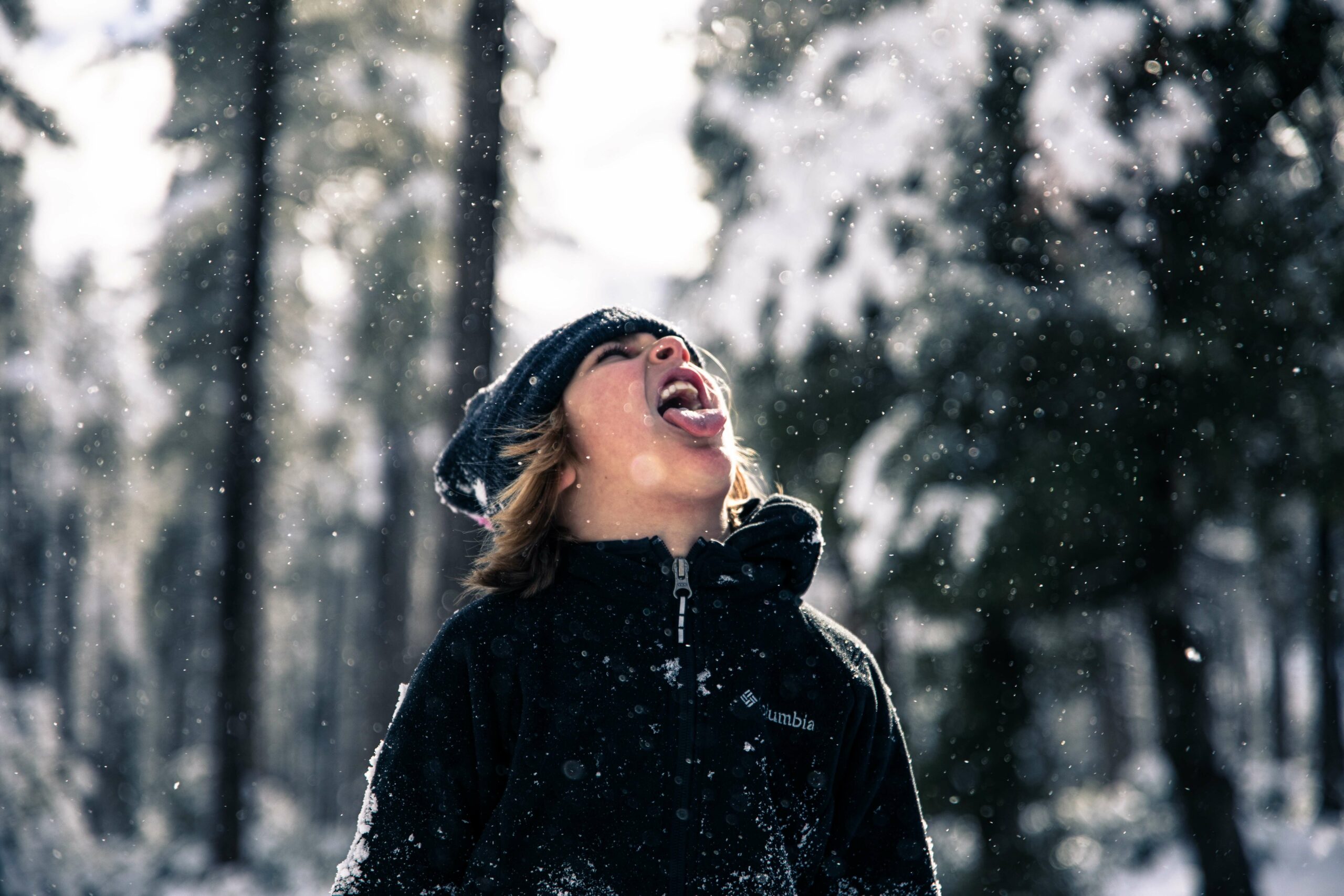 Young boy catching snowflakes on his tongue in the forest