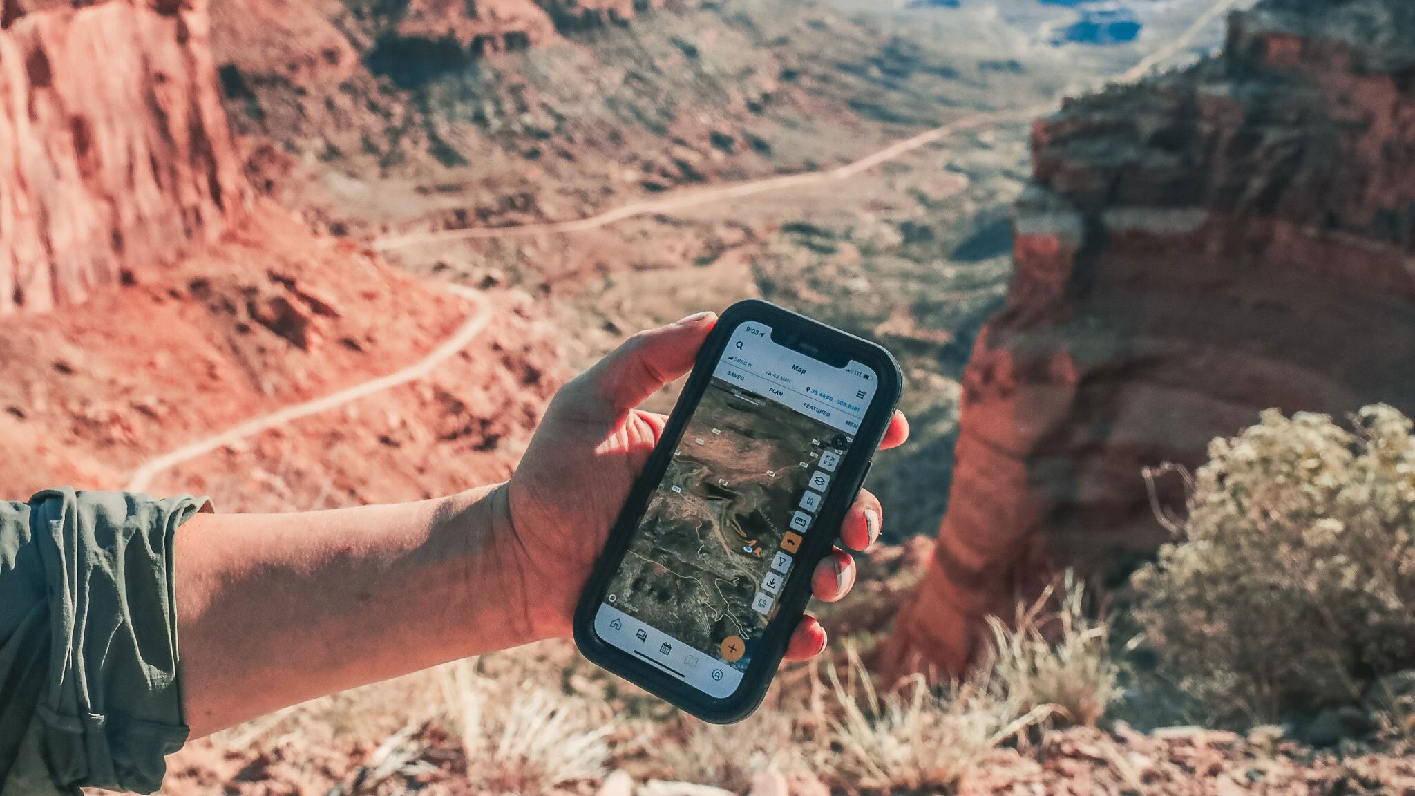 A hand holding a phone running Overland Bound One over a red-rock canyon trail